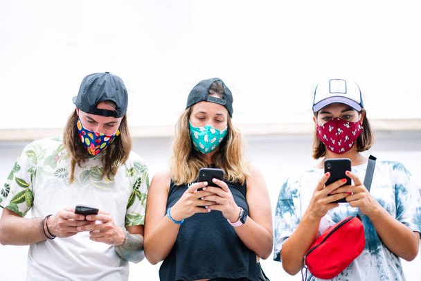Grupo de amigos charlando con el teléfono inteligente y el uso de máscara al aire libre - Foto, imagen
