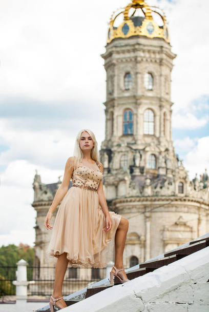 Full body portrait of a young beautiful blonde woman in beige dress against the background of the Temple of the Sign of the Most Holy Mother of God in Dubrovitsy - Zdjęcie, obraz