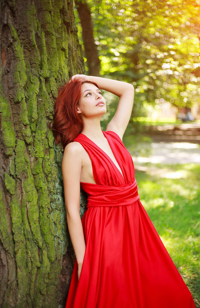 Приваблива молода дівчина, леді в довгій червоній сукні в літньому лісовому парку, модна жінка на відкритому повітрі в природі
 - Фото, зображення