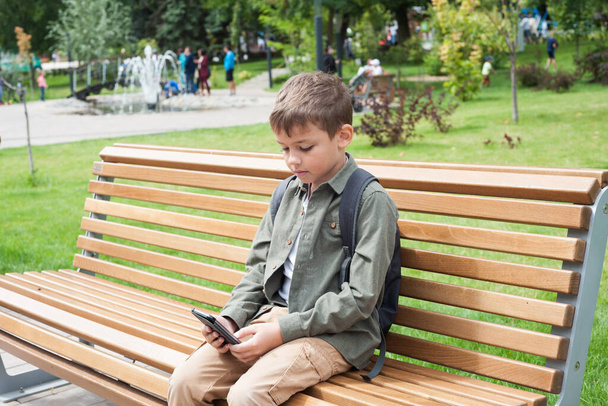 un ragazzo è seduto su una panchina con un telefono in mano - Foto, immagini