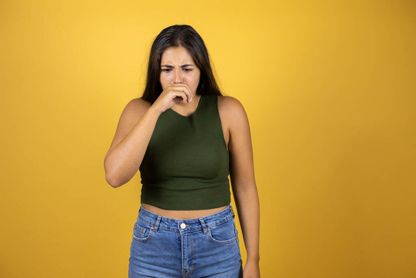 Young beautiful woman standing over yellow isolated background with her hand to her mouth because she's coughing - Fotó, kép