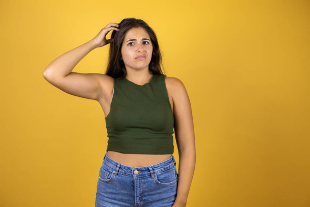 Young beautiful woman over isolated yellow background confuse and wonder about question. Uncertain with doubt, thinking with hand on head - Photo, Image
