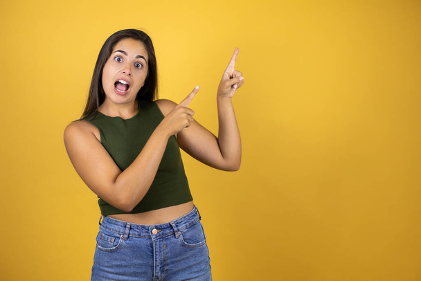 Young beautiful woman standing over yellow isolated background surprised, smiling and pointing his fingers - Photo, Image