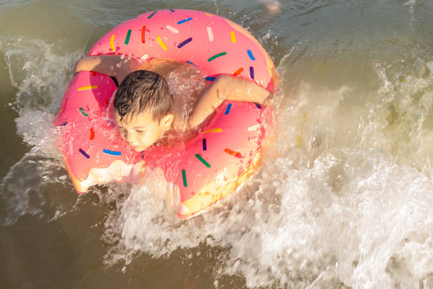 5-річний хлопчик купається в морі в рятувальному кільці на сонячний день
 - Фото, зображення