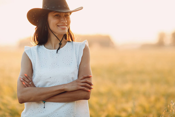 Женщина-фермер в ковбойской шляпе на сельскохозяйственном поле на закате с солнечной вспышкой - Фото, изображение