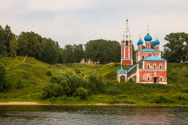 Tutaev, Yaroslavl region / Russia-July, 29, 2020: Red Kazan Church on the high hilly Bank of the Volga river on a cloudy summer day and space for copying - Foto, imagen