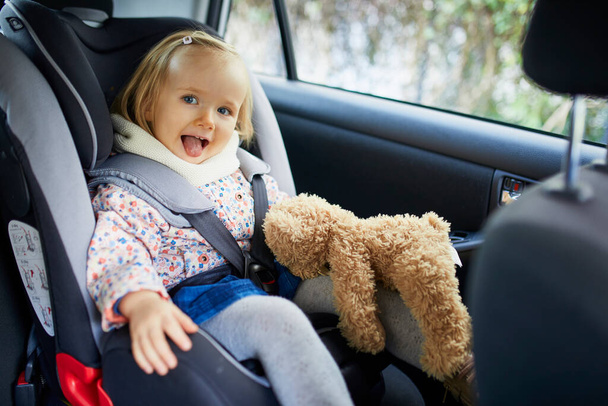 Adorable toddler girl in modern car seat with her favorite stuffed toy. Little kid traveling by car. Child safety on the road. Trip with a baby - Foto, Bild
