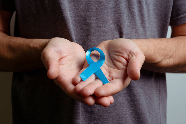 Man holding light blue ribbon. Awareness ribbon. - Фото, зображення