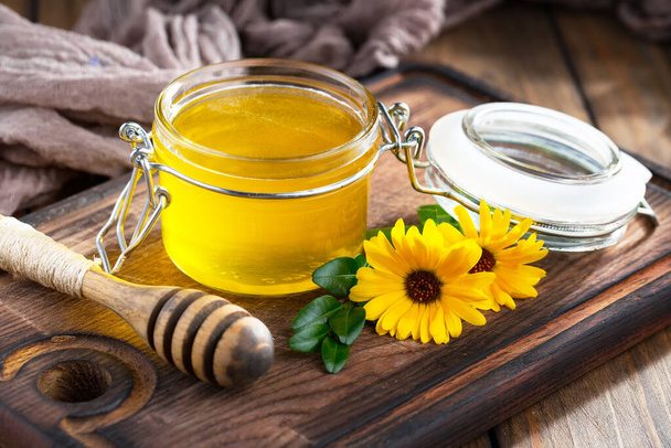 Bee honey in a jar with a flower, on the old background. - 写真・画像