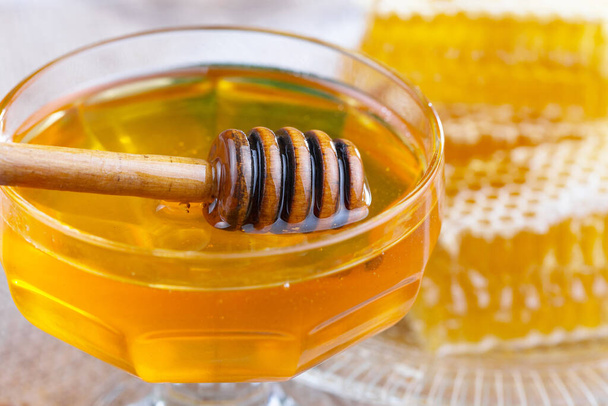 The honey flows slowly from the stick onto the honeycomb. - Foto, Imagen