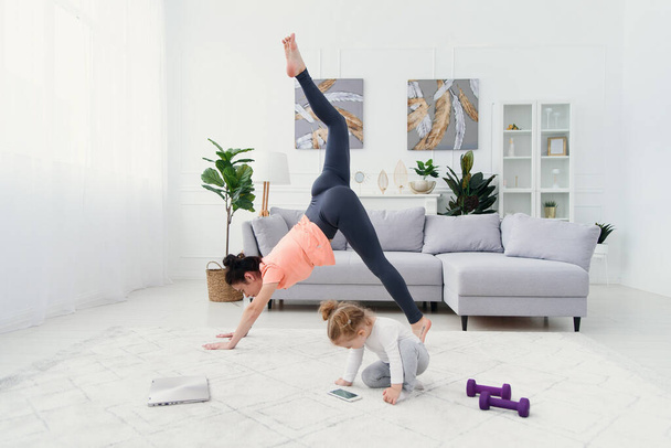 Young mom making stretching exercises and practicing yoga with baby girl at home. Health care and sports concept. - Valokuva, kuva