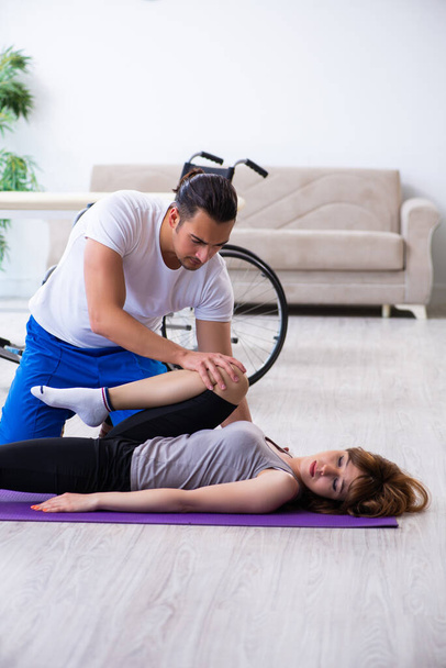 Male physiotherapist doing exercises with injured woman on floor - Fotoğraf, Görsel