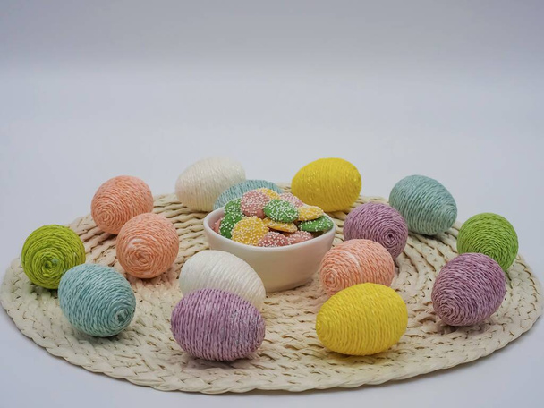 Corde décorée d'œufs de Pâques sur un napperon rond crème avec un bol blanc de bonbons au centre. Couleurs pastel parfaites pour Pâques et le printemps. - Photo, image