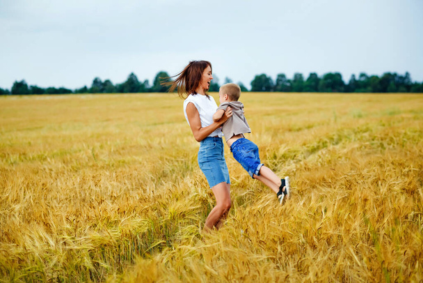 Onnellinen perheen äiti ja poika kesäisellä vehnäpellolla. Nainen kietoo kätensä pojan ympärille.. - Valokuva, kuva