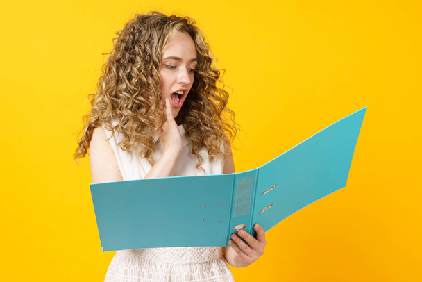 A young woman holds folders with documents in her hands. Reads and wonders. Isolated on yellow background - Foto, Imagem