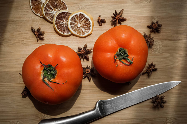 Čerstvá rajčata na dřevěném stole s ovocným nožem a sušenými plátky citronu shora - Fotografie, Obrázek
