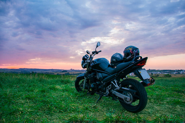 Um capacete de motocicleta preto colocado no assento de uma motocicleta preta estacionada na rua com uma paisagem natural. - Foto, Imagem