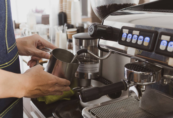 young man using coffee maker machine to make frothy milk cream. barista and cafe concept - Fotoğraf, Görsel