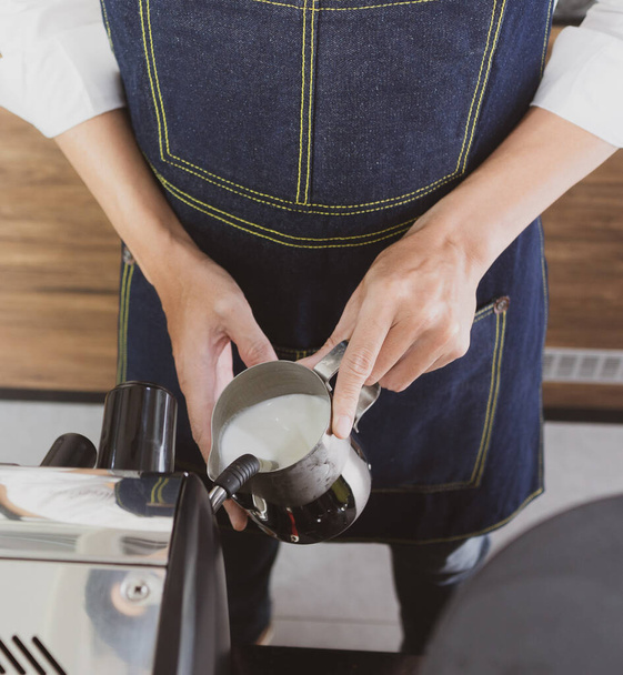 young man using coffee maker machine to make frothy milk cream. barista and cafe concept - Fotó, kép
