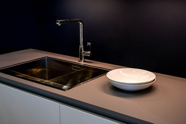 Lavello nero e acqua di rubinetto in cucina. L'interno della sala da cucina dell'appartamento. Elettrodomestici. Piatti bianchi - Foto, immagini
