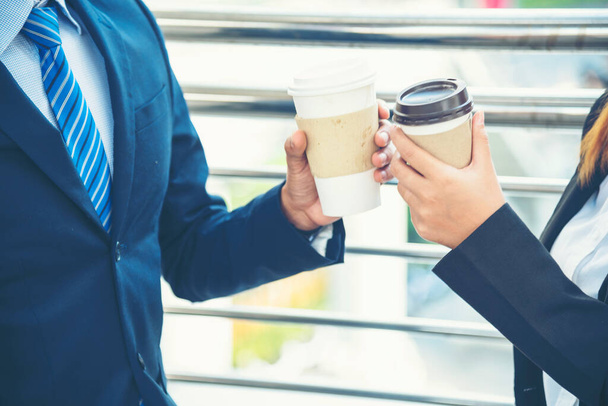 Молодые азиатские бизнесмены улыбаются и расслабляются, держа чашку кофе перед работой. Пара любовников любят пить кофе вместе в современном городе. Деловые люди, держащие чашку кофе в офисе - Фото, изображение
