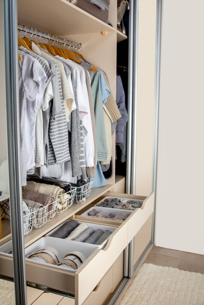 Wardrobe with perfect order clothes in blue and light shades on the hangers and things in containers. The concept of organizers and cleanliness in the house - Foto, Imagen