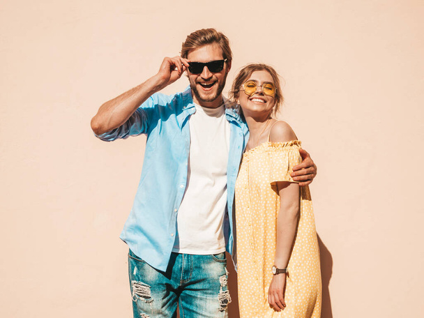 Portrait of smiling beautiful girl and her handsome boyfriend. Woman in casual summer dress and man in jeans. Happy cheerful family. Female having fun in the street near wall - Foto, imagen