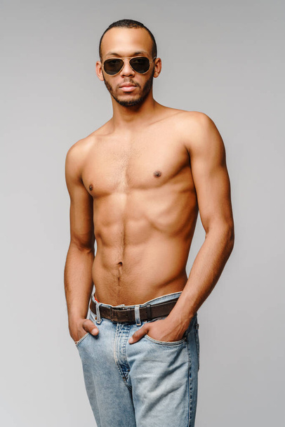Sexy joven musculoso africano americano hombre sin camisa con gafas de sol sobre fondo gris claro - Foto, imagen
