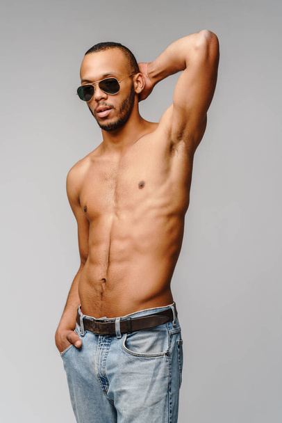 Sexy young muscular african american man shirtless wearing sunglasses over light grey background - Zdjęcie, obraz
