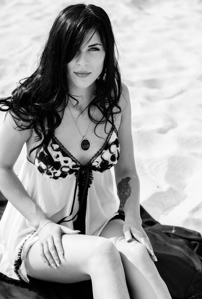 Sexy babe in a night black and white negligee and fabrics in the desert on the sands. Relaxed and erotic gorgeous lady posing at the beach - Photo, image