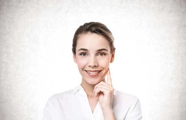 Portrait of young smiling European businesswoman standing near concrete wall and looking at camera - Photo, Image