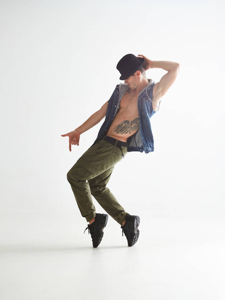 Young man dancer in hat dancing moonwalk in studio isolated on white background. Dance school poster - Фото, изображение