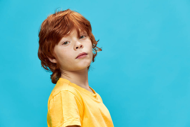  Рыжий ребенок в жёлтой футболке на синем фоне - Фото, изображение