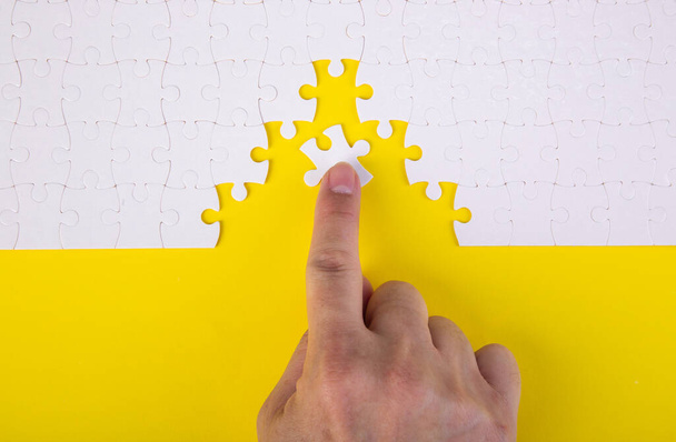 Hand putting the a piece of white jigsaw puzzle on color background and place for your content - Photo, Image
