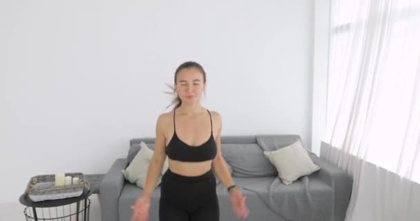 Woman is doing jumping jeg exercise on carpet in living room, camera moves away. - Záběry, video