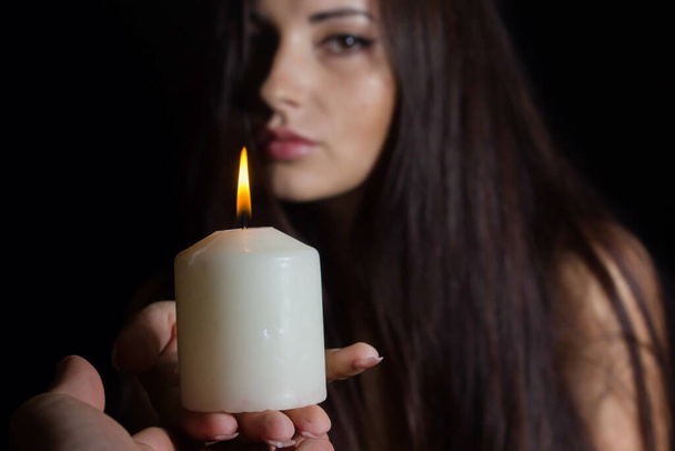Chica con velas encendidas. Una morena sobre fondo negro entrega una vela blanca a otra. Misticismo y adivinación. magia negra - Foto, imagen