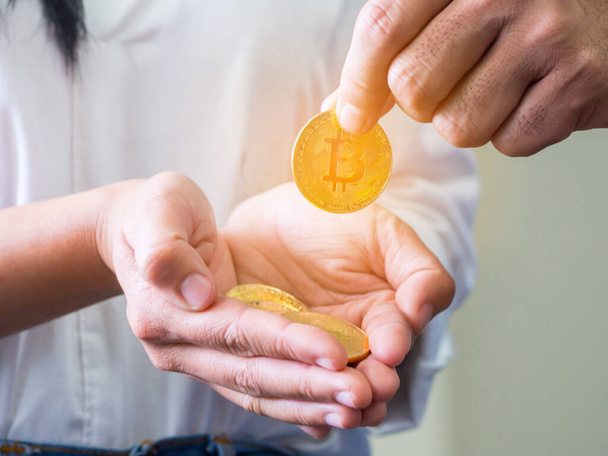 Die Hand eines Mannes hob eine goldene Bitcoin-Münze von der Handfläche einer Frau mit mehreren Bitcoins in der Hand auf weißem Hintergrund auf.. - Foto, Bild