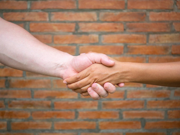 Крупный план рукопожатия между мужчиной и женщиной на кирпичном фоне. Концепция командной работы и единства - Фото, изображение