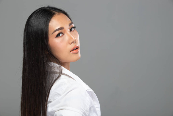 Portrait of Fashion 20s Asian Woman hat schöne schwarze lange glatte Haare, sie trägt weißes Hemd Blick in die Kamera über grauen Hintergrund isoliert Kopierraum - Foto, Bild