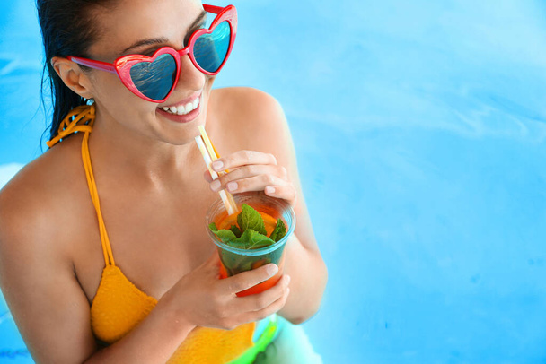 Woman with glass of refreshing drink in swimming pool, closeup - Foto, imagen