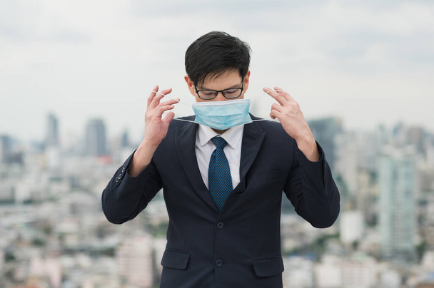 Joven guapo asiático hombre de negocios de pie usando máscara de proteger la contaminación y el virus en la construcción de ciudades urbanas fondo. - Foto, imagen