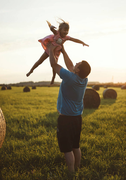 A happy child runs through a field of haystacks at sunset - 写真・画像