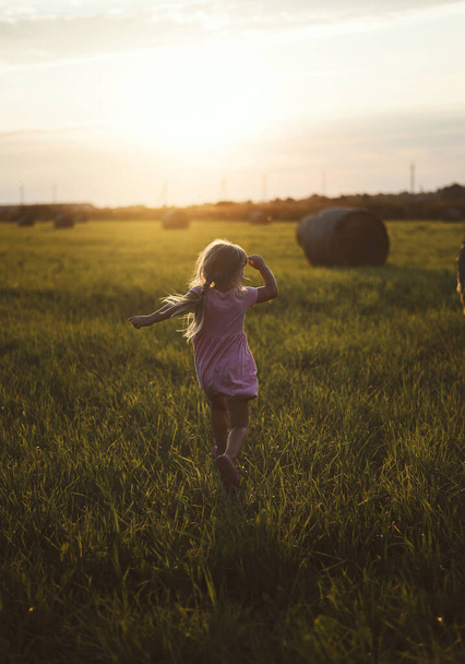A happy child runs through a field of haystacks at sunset - Photo, Image