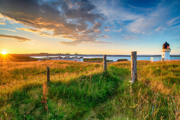 スコットランドの外へのヘブリディーズ諸島のルイス島のStornoway近くのArish Pointの灯台と沿岸警備隊のコテージの上の美しい夕日 - 写真・画像