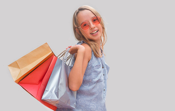 Ребенок в очках на сером фоне. девушка держит сумки - Фото, изображение