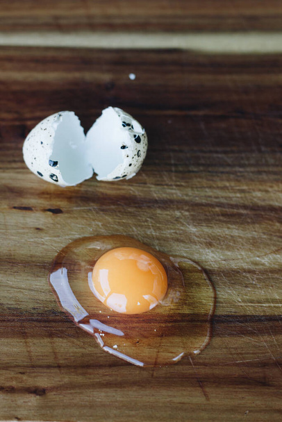 A vertical shot of a smashed quail egg on a wooden table - Photo, image