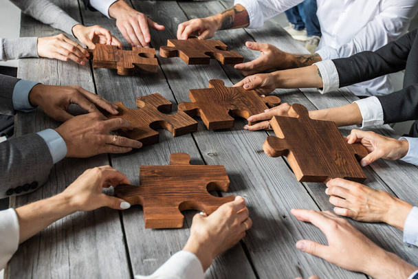 Business people team sitting around meeting table and assembling wooden jigsaw puzzle pieces unity cooperation ideas concept - Foto, Imagem