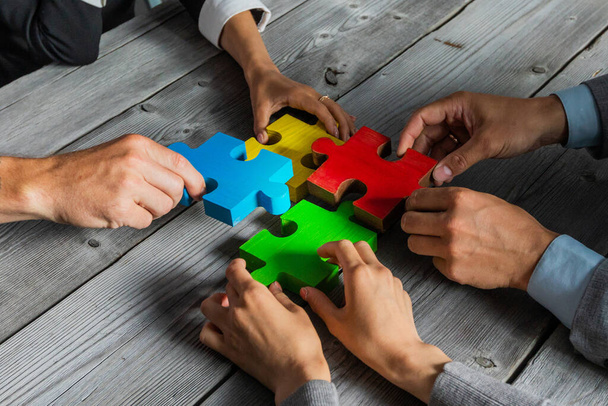 Business people team sitting around meeting table and assembling color jigsaw puzzle pieces unity cooperation ideas concept - Foto, Imagem