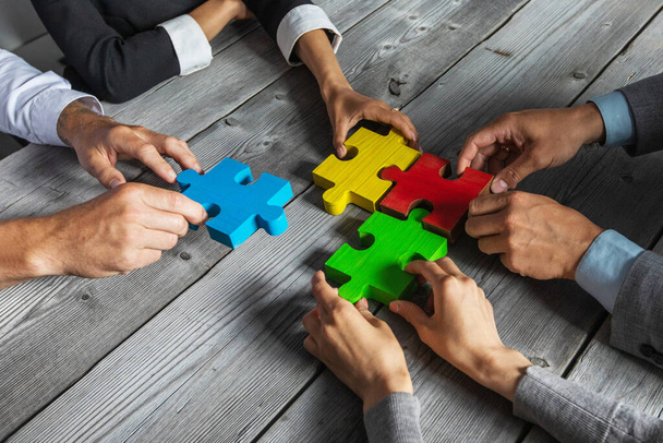 Business people team sitting around meeting table and assembling color jigsaw puzzle pieces unity cooperation ideas concept - Fotoğraf, Görsel