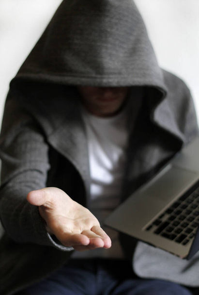 A vertical shot of a hooded man near a laptop holding his hand out- cybersecurity concept - Foto, immagini